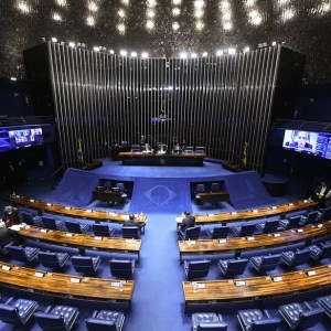 Foto do plenário do Senado Federal, com fileiras de cadeiras e microfones aos lados e a mesa diretora no centro