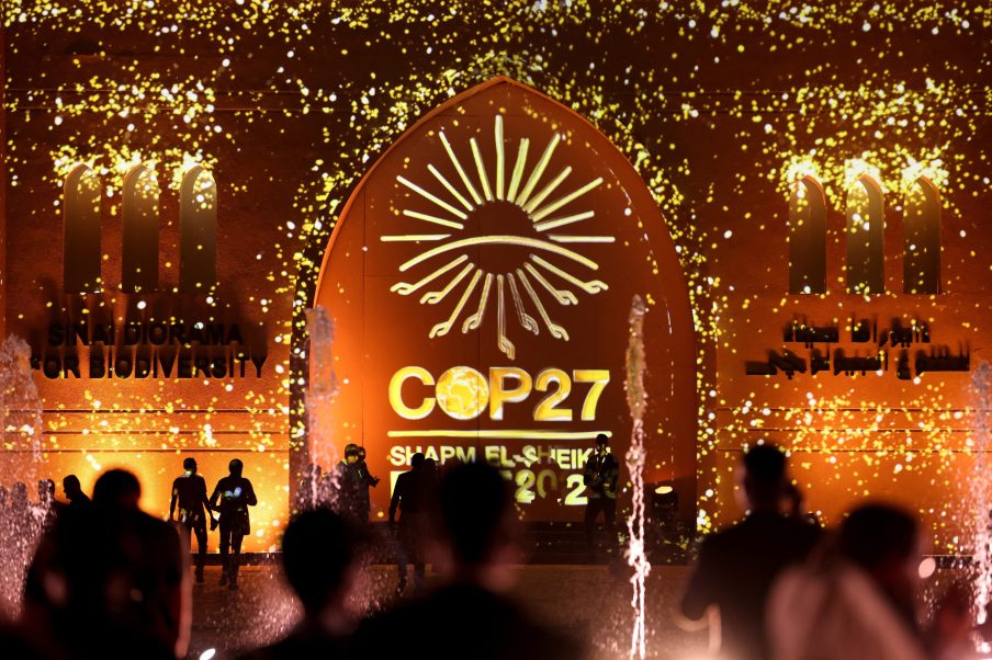 Pessoas passam em frente a uma parede iluminada com o sinal da COP27 durante a cúpula do clima COP27, em Sharm el-Sheikh, Egito, 10 de novembro de 2022