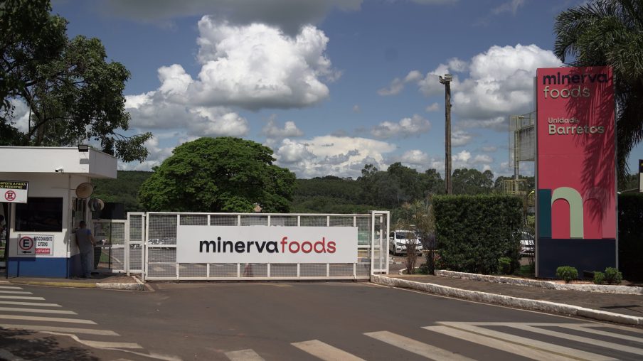 Foto de portão de planta industrial da Minerva Foods (BEEf3) em Barretos. O portão tem o logo da companhia.