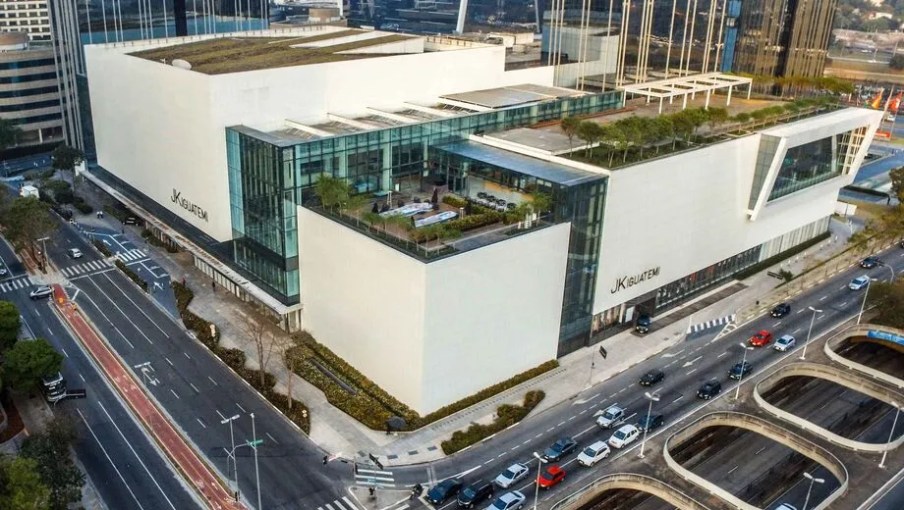 Imagem com a vista aérea de um shopping, com algumas torres claras e ruas em volta.