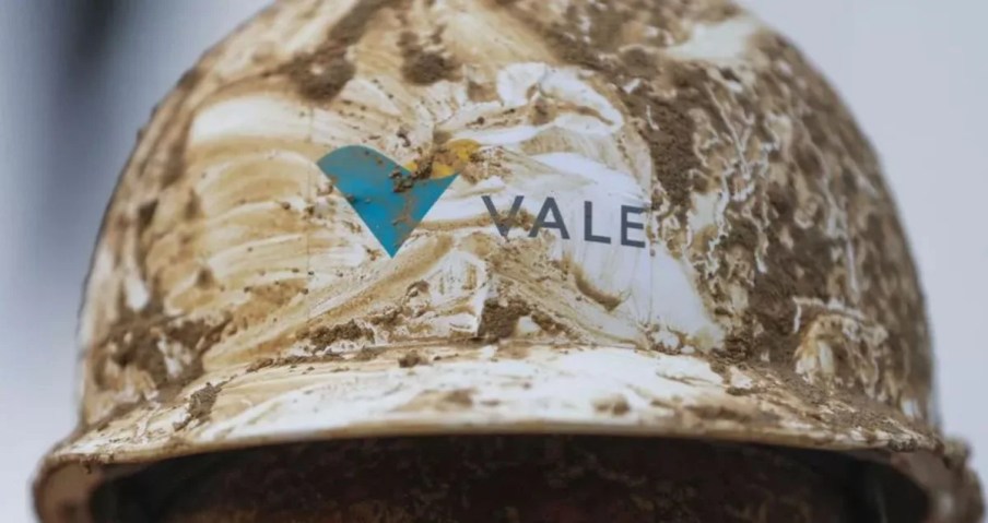 Foto de um capacete da Vale (VALE3) sujo de lama, com o logo da empresa. A matéria explica como o minério de ferro está com preços estáveis em 2024.