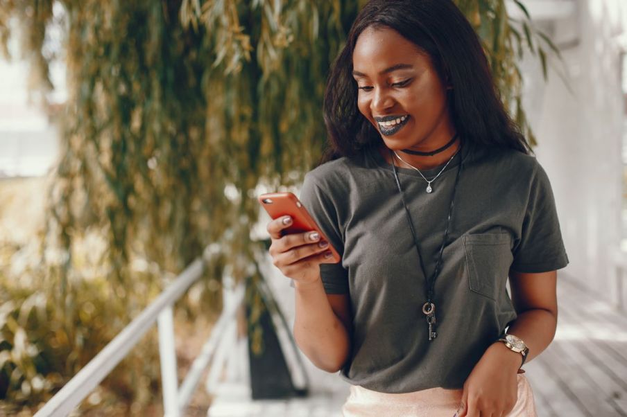 Imagem de uma mulher negra sorrindo olhando para um celular.