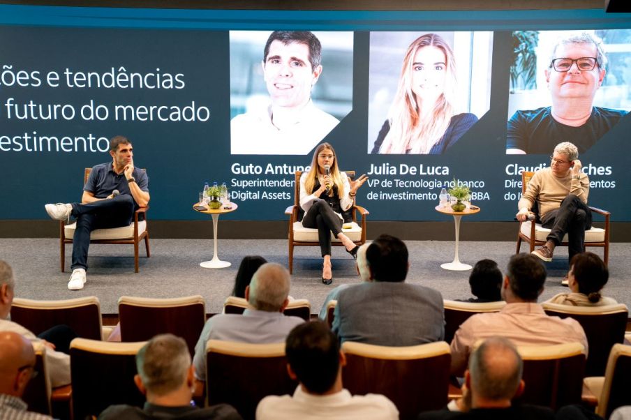 Foto para ilustrar o painel de um evento sobre tecnologia nos investimentos. Nela há dois homens sentados ao lado de uma mulher loira.