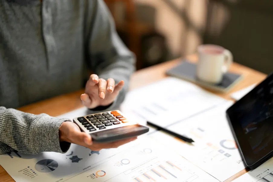 Imagem de uma pessoa com uma calculadora na mão e papéis sobre a mesa para ilustrar conteúdo sobre ETF renda fixa atrelado à inflação