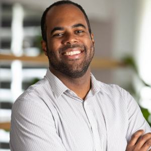 Foto do economista Felipe Oliveira, da MAG Investimentos. Ele é homem, negro e usa camisa social. É um dos entrevistados da matéria que explica como o Copom não deve cortar taxa Selic mesmo com queda do PIB do Brasil.