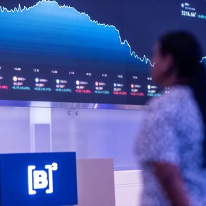 Foto de uma tela com diversos gráficos desenhados. Há uma mulher olhando para uma placa azul escrita B3.