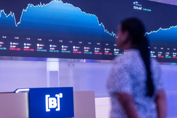 Foto de uma tela com diversos gráficos desenhados. Há uma mulher olhando para uma placa azul escrita B3.